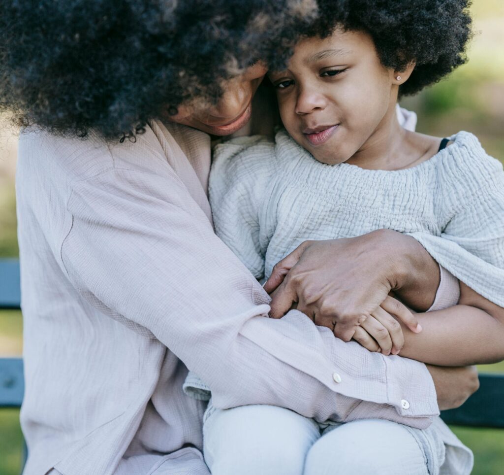 Tender moment between a mother and daughter embracing on a park bench.
