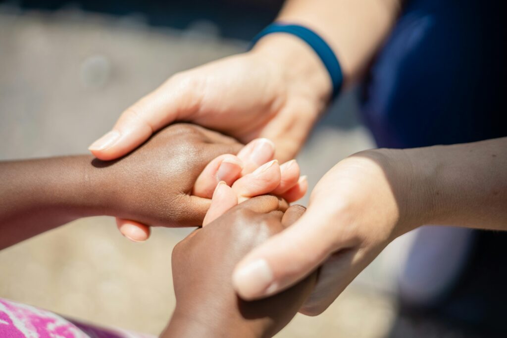Two pairs of diverse hands holding, symbolizing unity and empathy, close-up outdoor shot.
