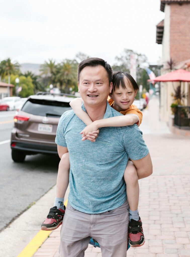 A joyful Asian father giving his child a piggyback ride on a city street.