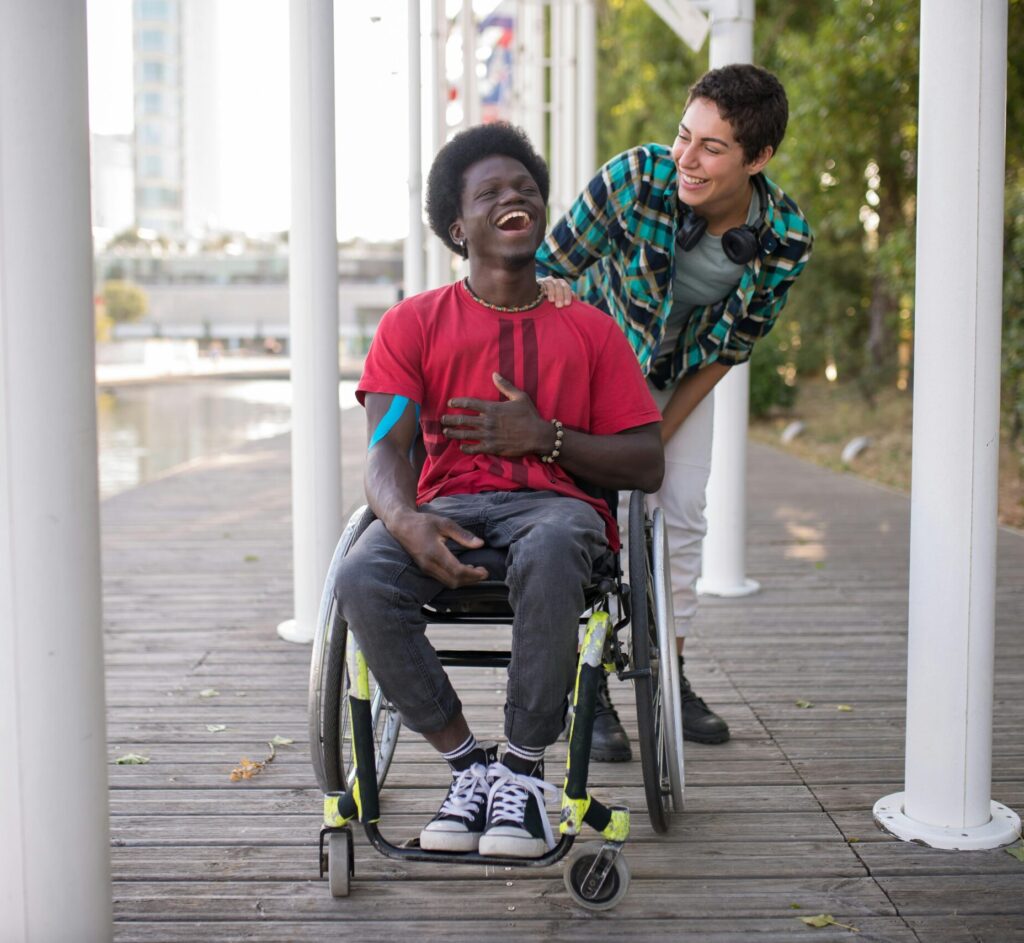 Two friends, one in a wheelchair, sharing a joyful moment outdoors in Portugal.